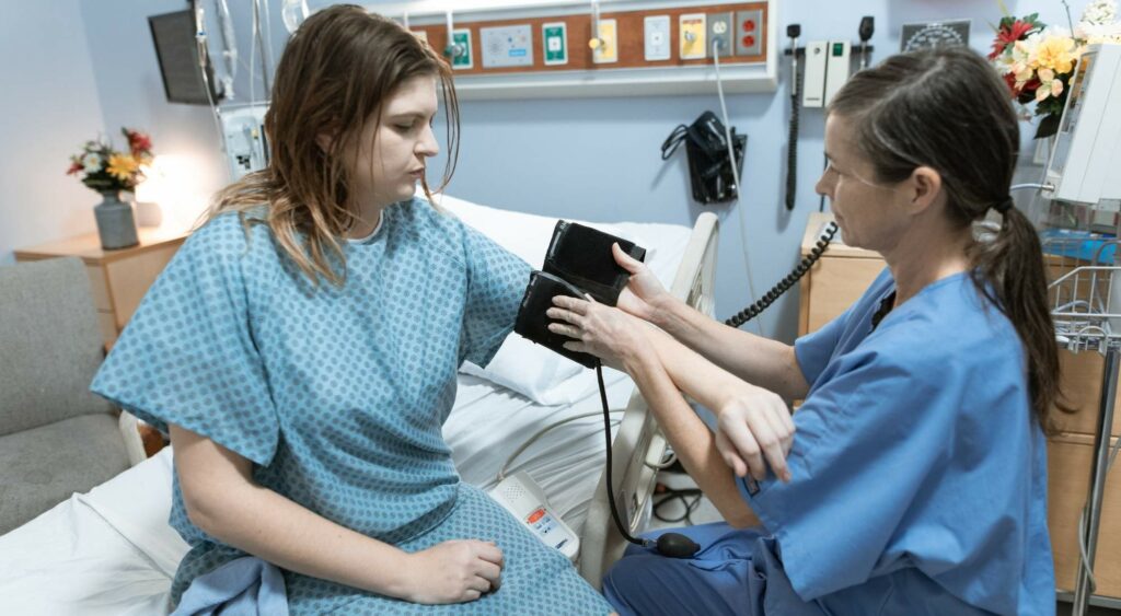 Nurse taking patient's blood pressure in hospital room, travel nursing expectations.
