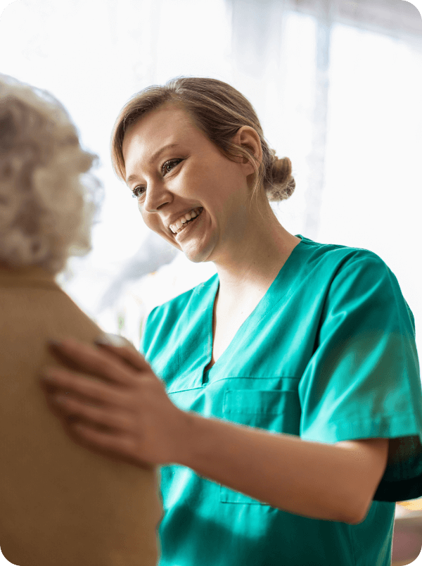 Smiling nurse in green scrubs caring for elderly patient, senior healthcare, compassionate caregiver interaction.