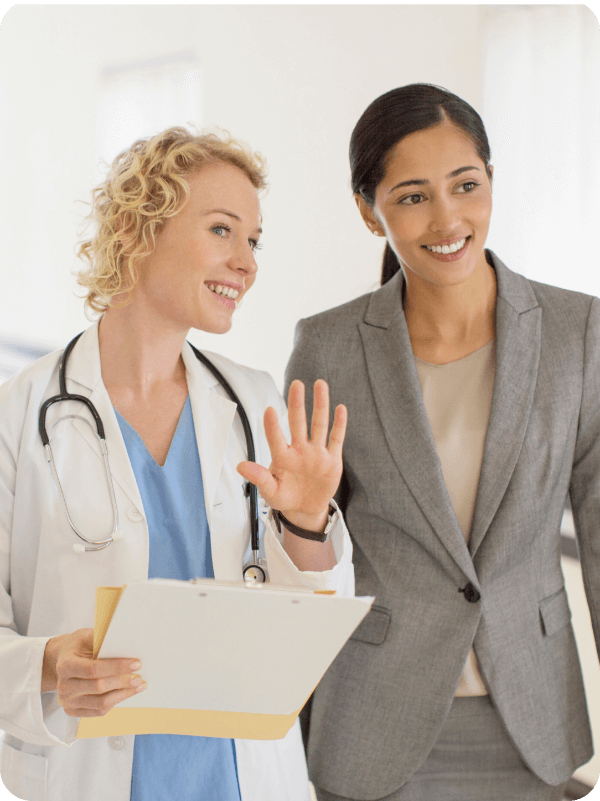 Two professionals, doctor and businesswoman, discussing healthcare plans in a medical facility hallway.